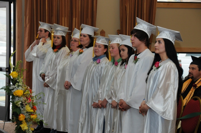 Students in white caps and gowns standing in a graduation ceremony