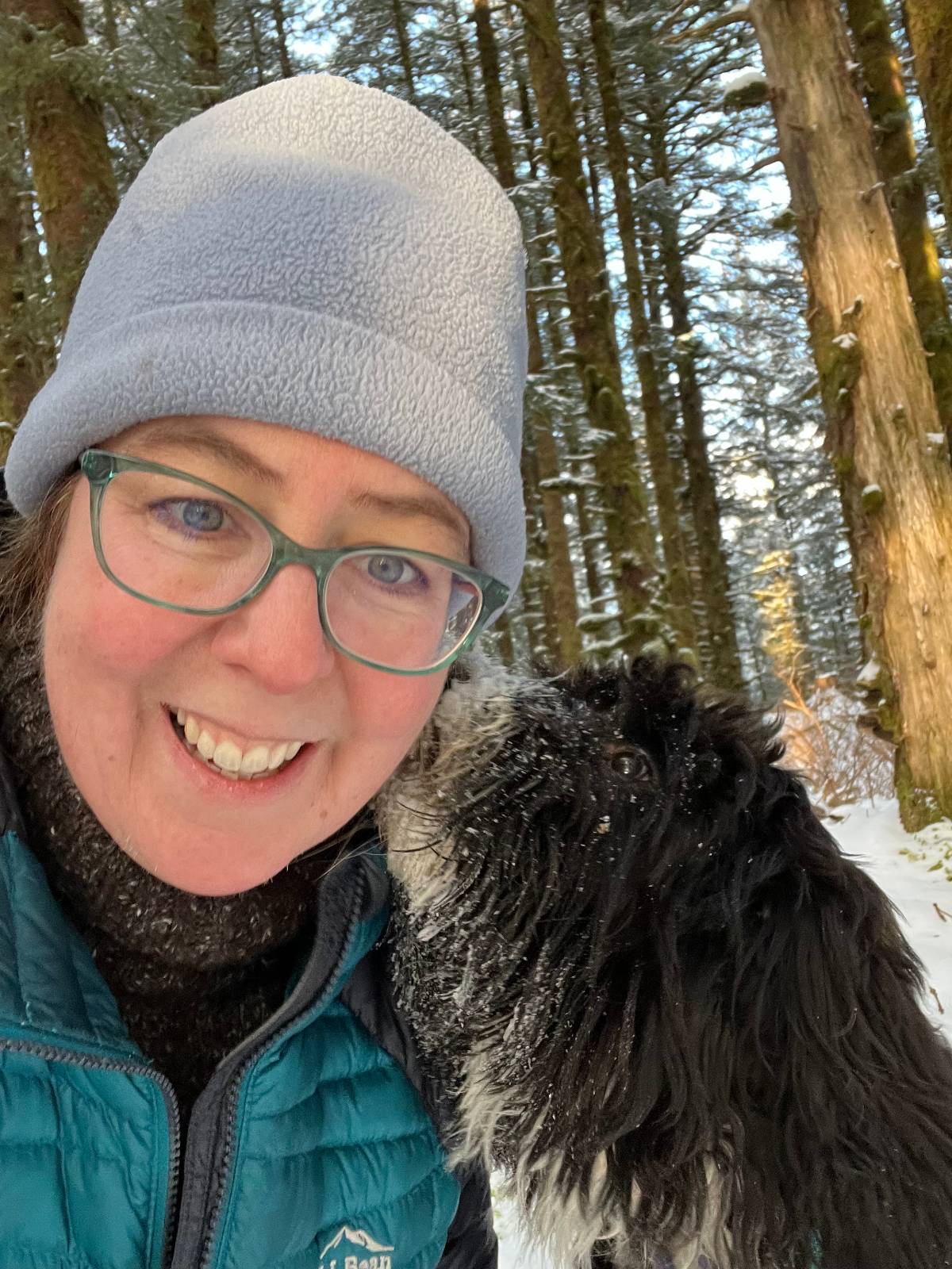 Cindy Trussell in the snow with a black and white dog licking her face