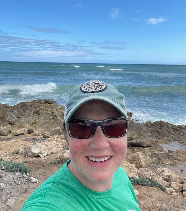 Kim Saunders posing for a selfie on a rocky beachwith the ocean behind her